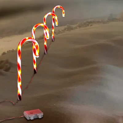 Four illuminated candy canes are placed in a snowy landscape.