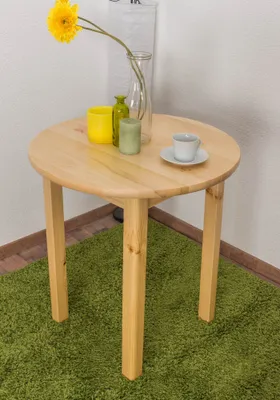 A round wooden table with decorative items on top, placed on a green rug in a corner.
