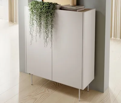 A modern, minimalist kommode with a hanging plant on top, placed in a well-lit room with wooden flooring.