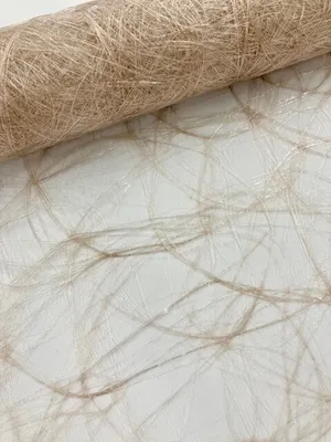 A close-up view of a roll of taupe-colored Sizoweb table runner with a textured, fibrous appearance, laid out on a white surface with a subtle web-like pattern.