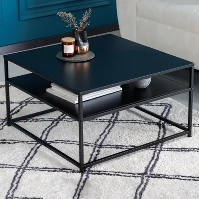 A modern black metal coffee table with a shelf, decorated with a candle and a vase, placed on a patterned rug.
