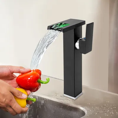 A person is washing red and yellow bell peppers under a black waterfall faucet with a green LED light.