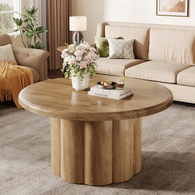A living room scene with a round coffee table in the foreground, a sofa and armchair in the background, and decorative items.