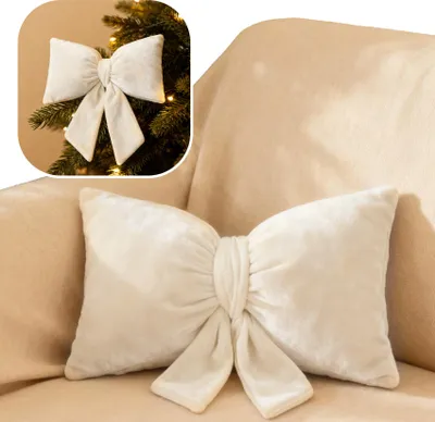 A cream-colored bow-shaped pillow is placed on a cream-colored sofa. A smaller inset image shows a similar bow on a Christmas tree.