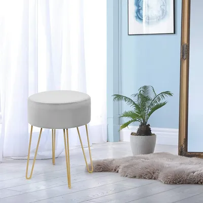 A round gray stool with gold legs is placed on a light-colored floor in a room with sheer white curtains and a blue wall.