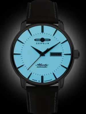 A close-up studio shot of a men's wristwatch with a black case and strap, and a light blue luminous dial.
