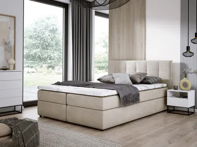 A bedroom scene featuring a beige boxspring bed with a mattress and pillows, set against a large window with a view of trees and a modern interior.