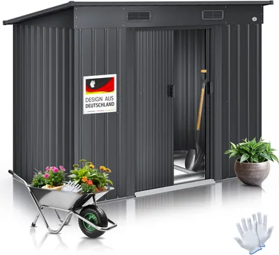 A dark gray metal garden shed with its door open, displaying gardening tools and plants. A wheelbarrow filled with flowers is in the foreground, and a potted plant and gloves are to the right. A German flag sticker is on the shed.