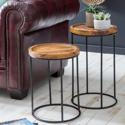 Two wooden nesting tables with black metal frames are placed next to a burgundy leather sofa.