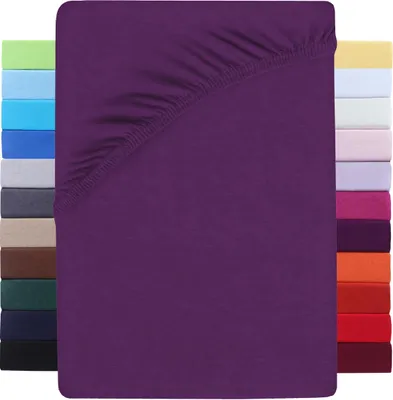 A folded purple fitted sheet is shown against a white background, with a stack of other colored sheets visible on the left and right sides.