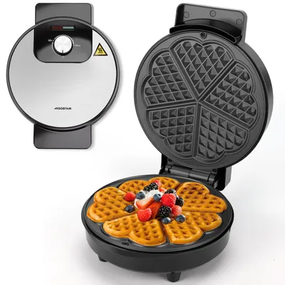A waffle maker is shown open with a freshly made heart-shaped waffle topped with berries and cream.
