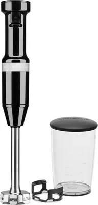 A black KitchenAid immersion blender with its accessories, including a beaker and a blade guard, is displayed against a white background.
