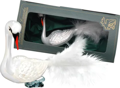 A white glass swan ornament with a clip is shown in front of its packaging, which also contains another swan ornament.