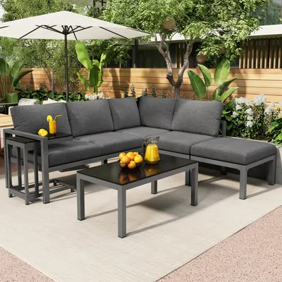 An outdoor patio scene with a gray sectional sofa, coffee table, and ottoman, set up for relaxation.