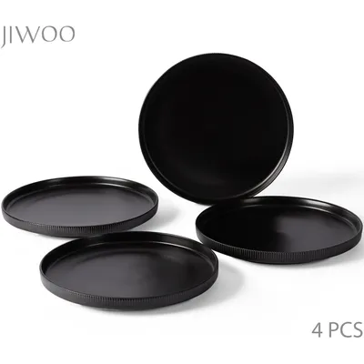 Four black ceramic plates are arranged on a white background. One plate is tilted upwards, showing its interior, while the other three are laid flat, with one slightly behind the other two.