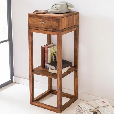 A wooden side table with a drawer and shelves, decorated with books and a vintage telephone.