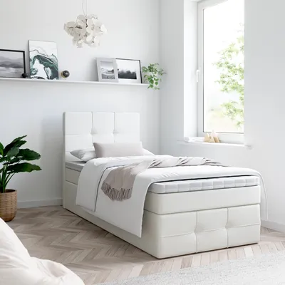 A white upholstered bed with a mattress and a throw blanket is shown in a bright, minimalist bedroom setting.
