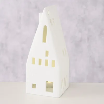 A white ceramic house-shaped lantern with cut-out windows, placed on a white surface against a textured light gray background.