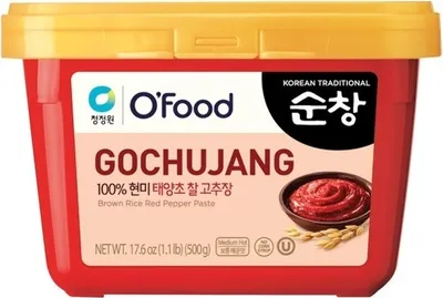A red plastic tub of Gochujang (Korean chili paste) with a yellow lid, set against a white background.
