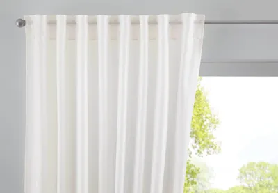 A white curtain hangs on a rod in front of a window with trees visible outside.