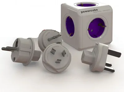 A white PowerCube with purple sockets and several interchangeable travel plugs are arranged around it on a white background.