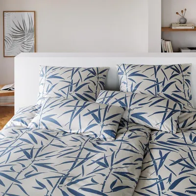 A neatly made bed with a blue and white bamboo leaf patterned duvet cover and pillows.