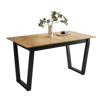 A dining table with a wood-look top and black metal legs, set against a white background. A vase with greenery and a book with a cup are placed on the table.