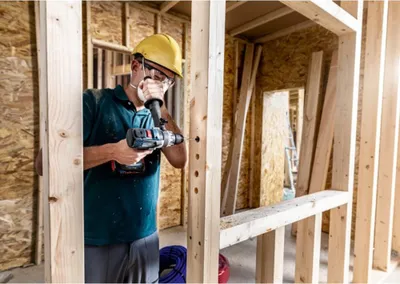 A construction worker is drilling holes in a wooden frame.