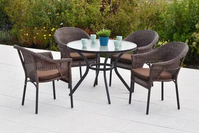 An outdoor patio set with a round table and four chairs, surrounded by greenery.