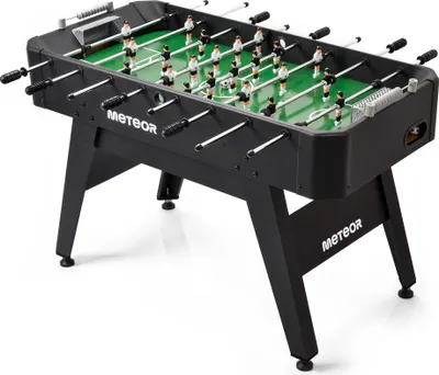 A black foosball table with green playing field and white and black player figures, shown from a slightly elevated side angle.