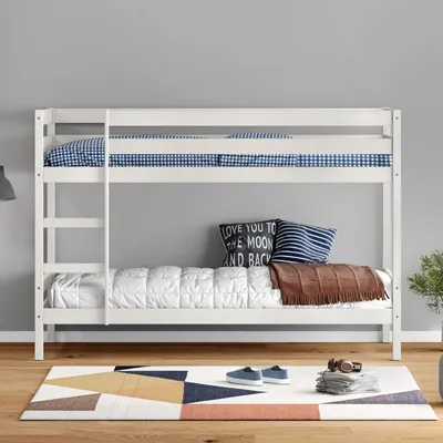 A white wooden bunk bed with bedding and pillows is shown in a room with a gray wall and a patterned rug on the floor.