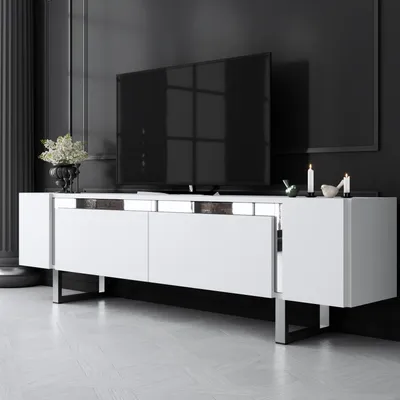 A modern white TV stand with silver accents and metal legs, placed in a minimalist room with a black wall and white floor.
