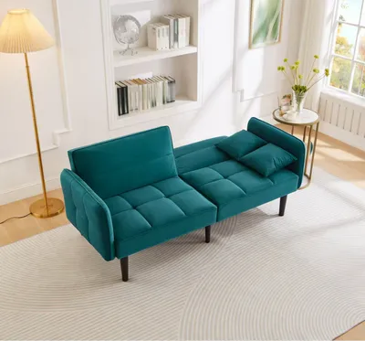 A teal futon sofa is shown in a living room setting with a floor lamp and a bookshelf.