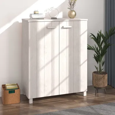 A white wooden cabinet with two doors is shown in a bright room, with sunlight casting shadows on it. A woven basket with books and a potted plant are placed next to the cabinet.