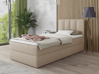 A bedroom scene featuring a beige boxspring bed with bedding and a headboard, next to a large window with green curtains and a potted plant. A floor lamp stands to the right.