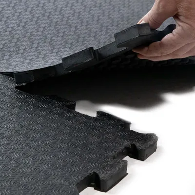 A hand is shown connecting two interlocking rubber stall mats.