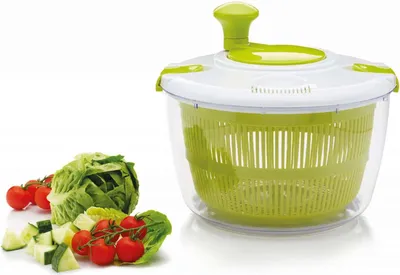 A salad spinner with some fresh vegetables next to it, on a white background.