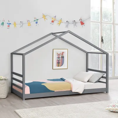 A child's bed with a house-shaped frame, decorated with a string of colorful figures and a framed picture on the wall.