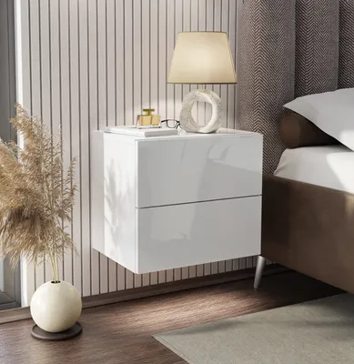A modern white bedside table mounted on a wall with vertical stripes, next to a bed with a textured headboard.