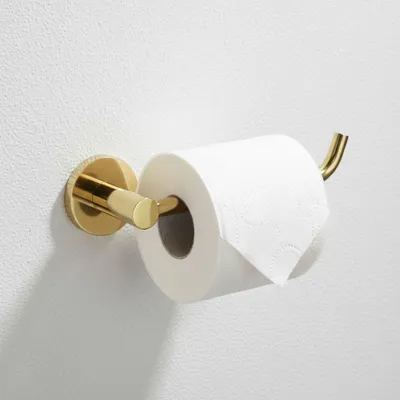 A gold toilet paper holder mounted on a white wall, with a roll of toilet paper on it.