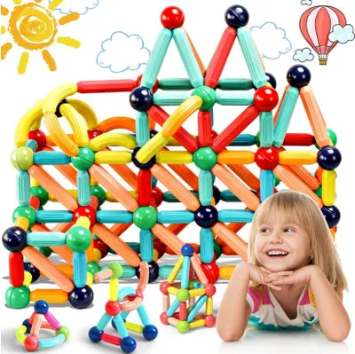 A young girl is lying down and smiling, with a large structure made of colorful magnetic building blocks behind her. There are also smaller magnetic block structures in the foreground. Decorative elements like a sun and clouds are in the background.