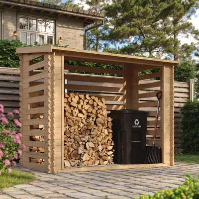 A wooden firewood storage shed filled with firewood, a trash can, and a shovel, set in a backyard garden.