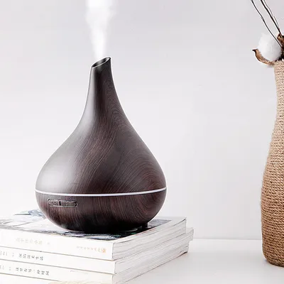 A dark brown aroma diffuser emitting mist, placed on a stack of books, with a decorative vase in the background.
