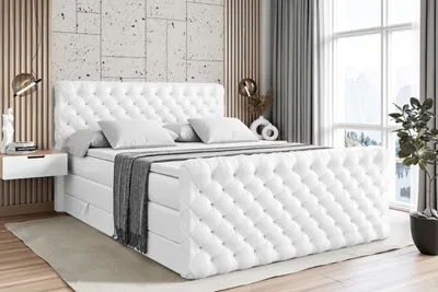 A bedroom scene with a large white upholstered bed as the main focus, set against a textured wall and wooden slats.