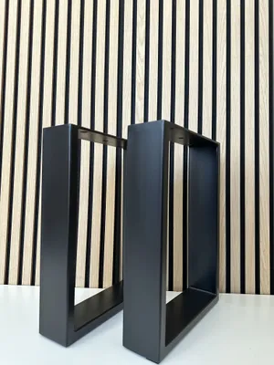 Two black metal table legs are displayed in front of a slatted wood and black panel wall.