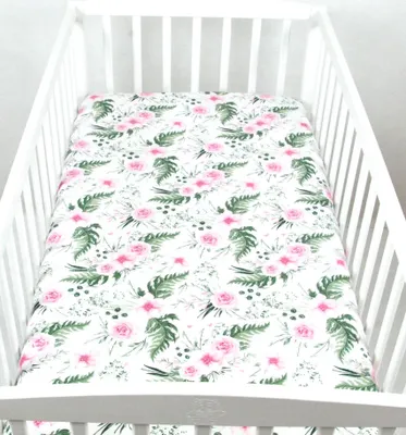 A floral patterned crib sheet is laid out inside a white crib.