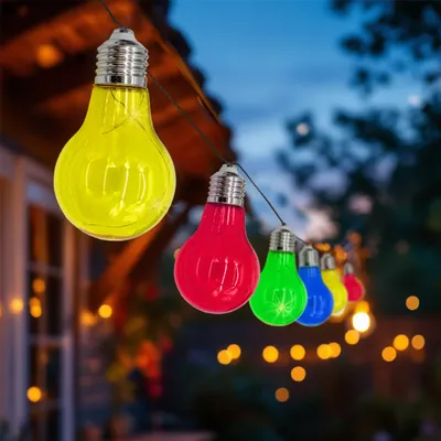 A string of colorful light bulbs hanging outdoors at dusk.