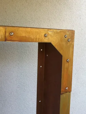 Close-up of a metal corner joint on a firewood rack, showing rivets and weathered metal.