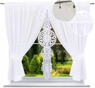 A white voile curtain with a decorative dreamcatcher panel hanging in front of a window with a garden view.