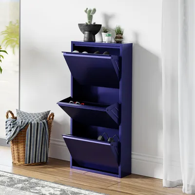 A dark blue shoe cabinet with three flip-down drawers is shown against a white wall. A wicker basket with a blanket and pillows is to the left, and a sheer white curtain is to the right.